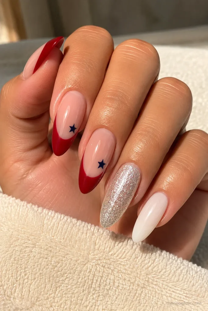 Acrylic 4th of July nails with a nude base, red tips, navy stars, and subtle glitter accents