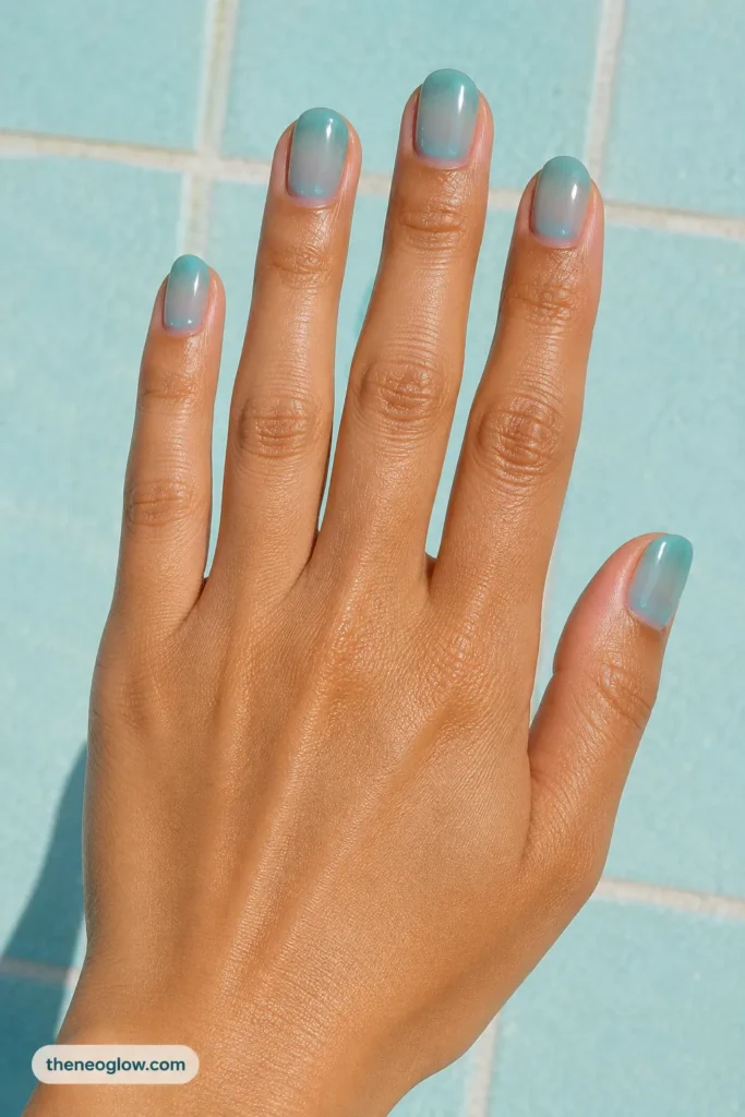 Translucent aqua jelly polish on short oval nails with a glossy, water-like finish on warm tan skin.
