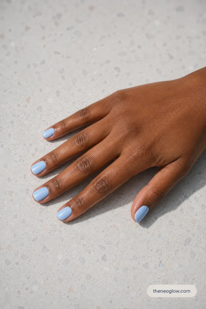 Creamy powder blue short oval nails with a glossy finish on rich brown skin with cool-neutral undertones.