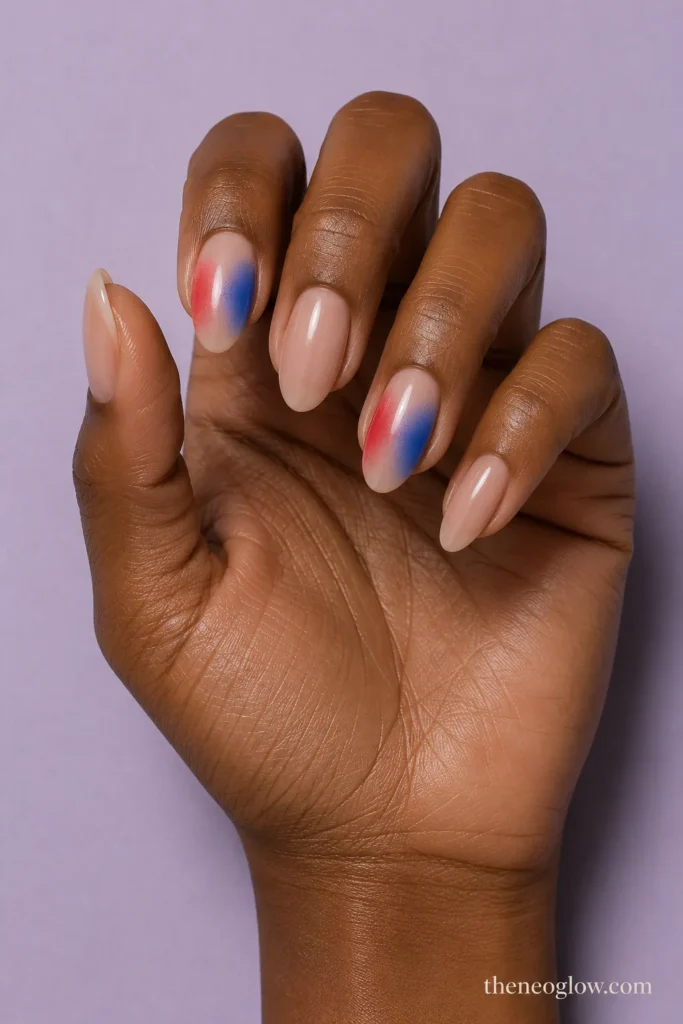 Medium almond nude nails with softly blended red and cobalt split-halo accents on deep brown skin.