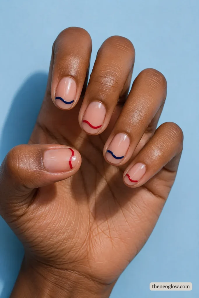 Short oval nails with single slim red and navy wave tips alternating across a transparent neutral base.
