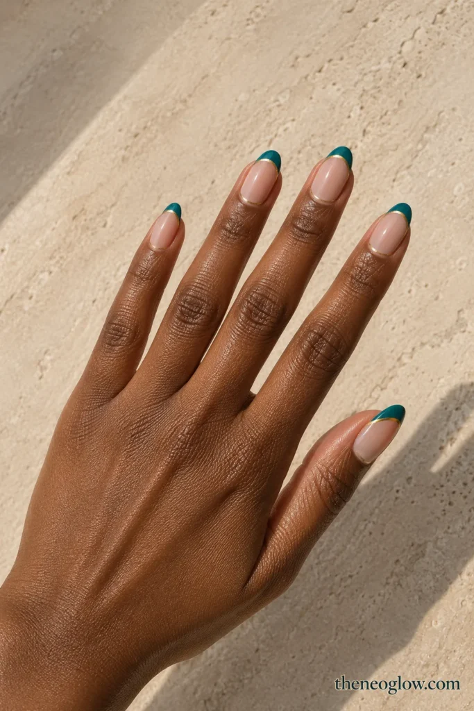 Medium almond nails with sheer nude bases, glossy teal French tips, and ultra-thin gold edging.