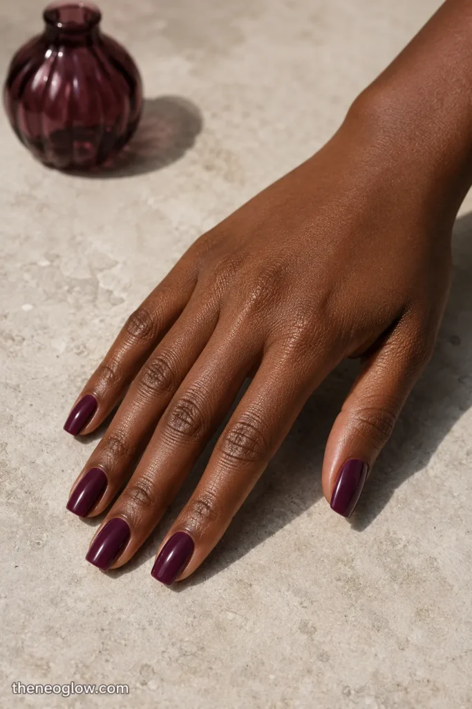 Glossy blackberry-plum polish on medium soft-square nails with visible berry-purple depth on deep brown skin.