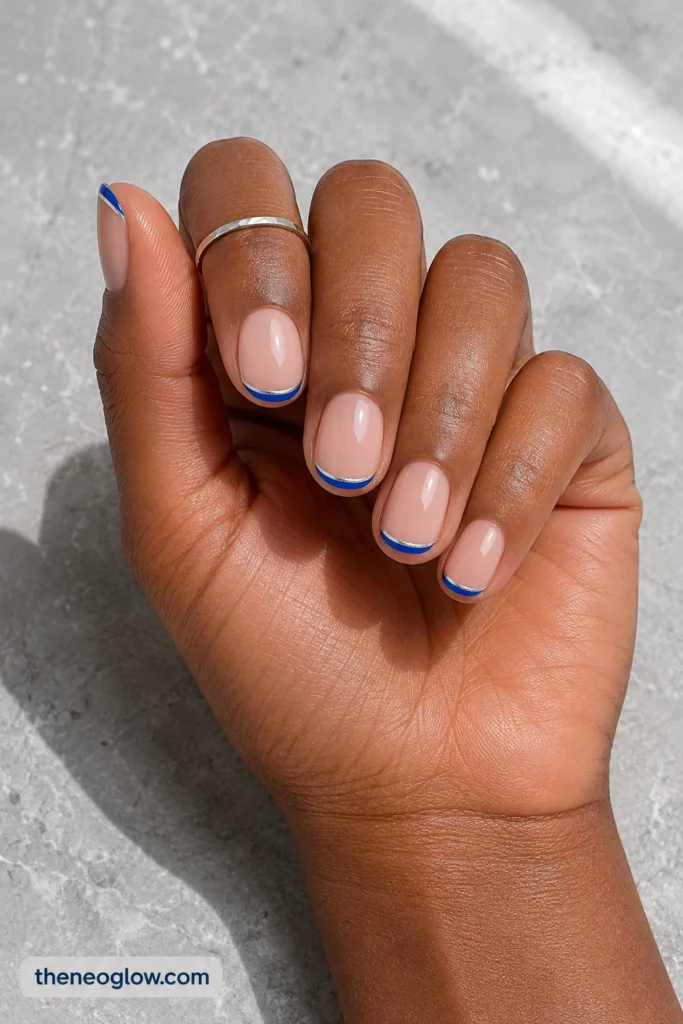Short oval nails with royal blue micro-French tips and fine silver outlines on deep brown skin.