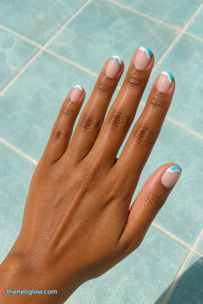 Short oval nails with sheer nude bases and irregular aqua-and-white splash French tips on rich brown skin.