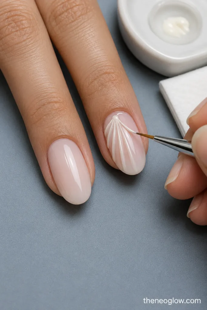 A fine nail-art brush forming pale shell ridges on a sheer pink oval nail at a salon workstation.