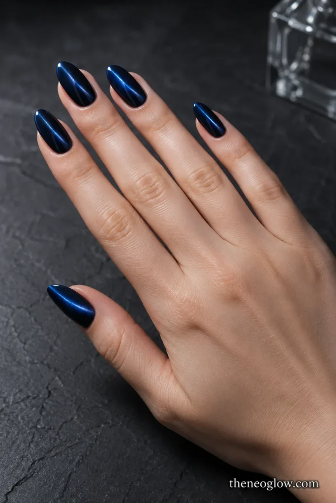 Medium almond nails with deep navy magnetic cat-eye polish and narrow reflective beams on light skin.