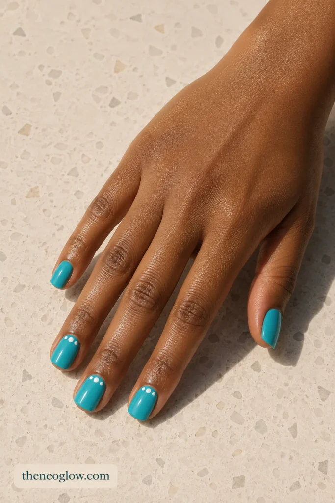 Short square turquoise nails with three tiny white cuticle dots on two accent fingers.