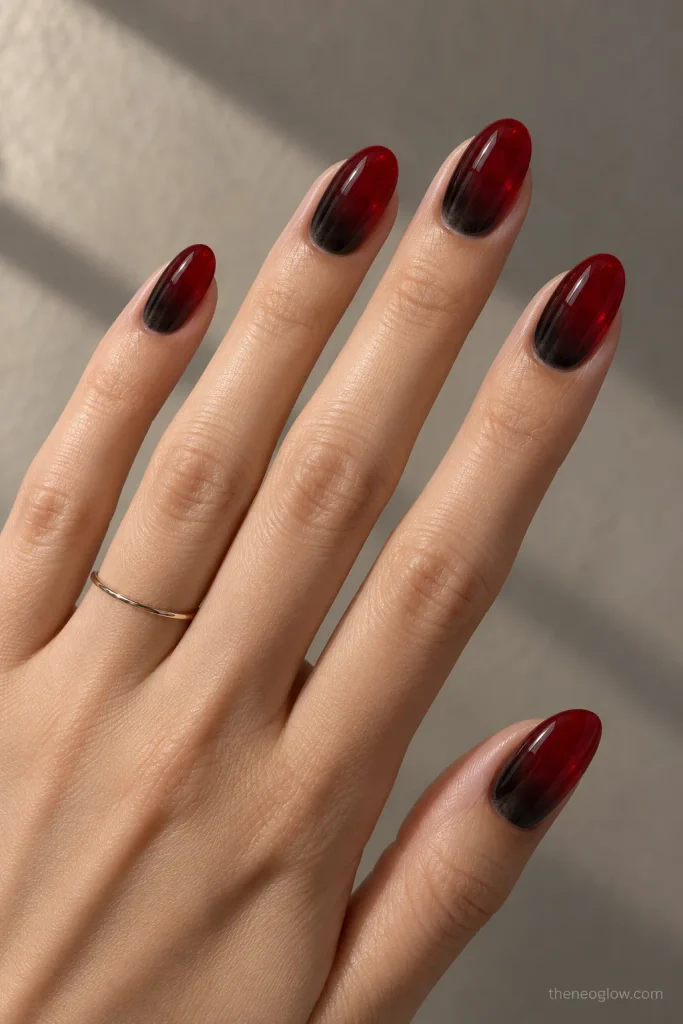 Glossy oval nails fading from a soft black cuticle shadow into luminous crimson.