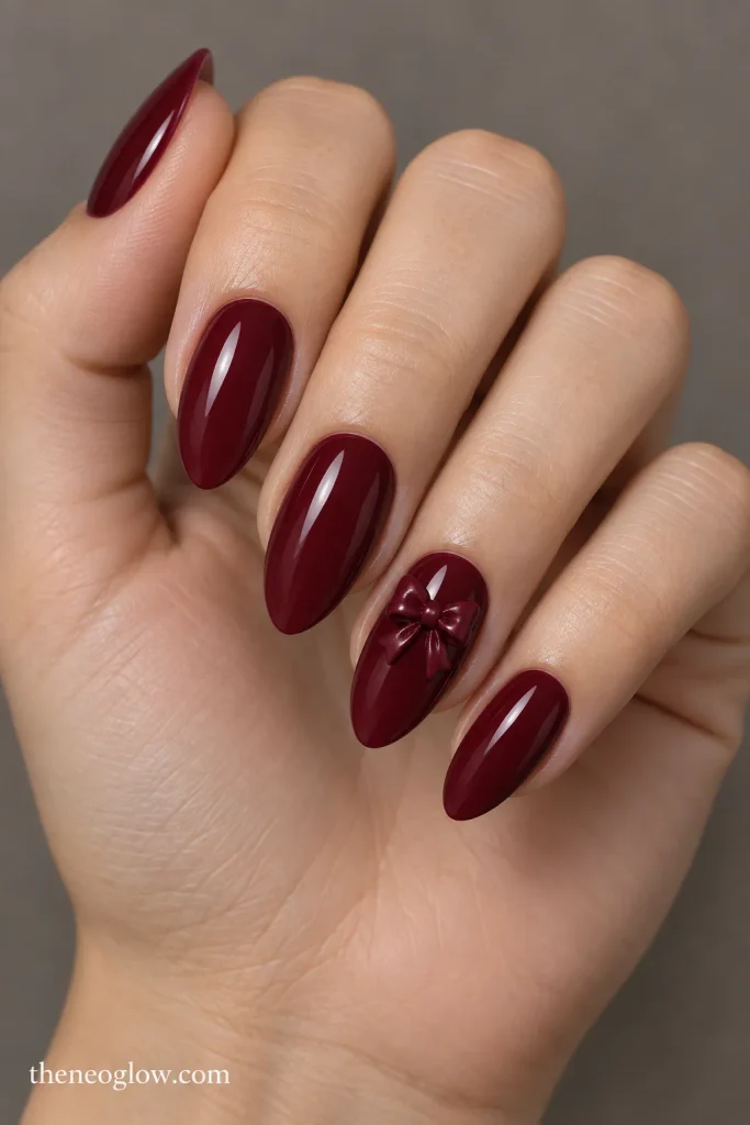 Glossy burgundy almond nails with one small sculpted bow accent.