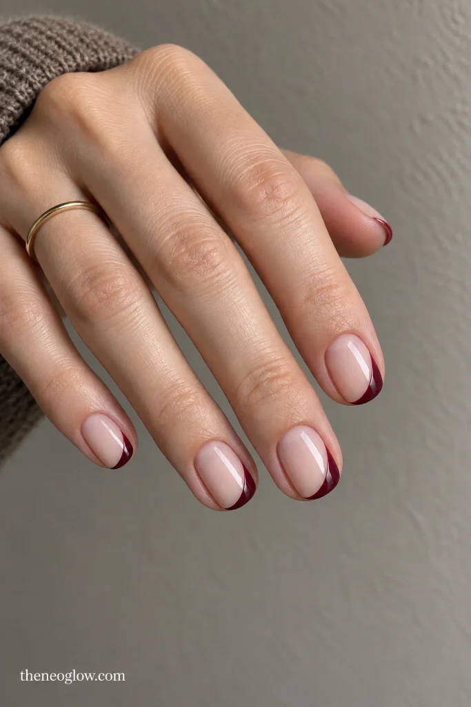 Sheer nude nails with asymmetric burgundy side-French sweeps and open negative space.