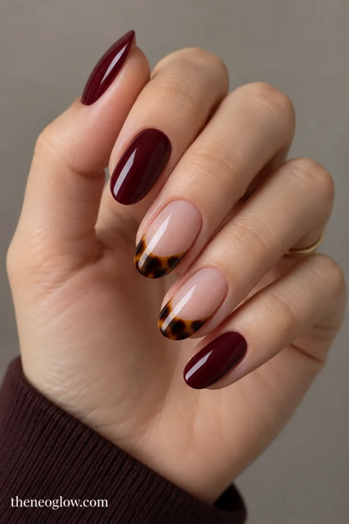 Glossy burgundy nails paired with two sheer tortoiseshell French-tip accent nails.