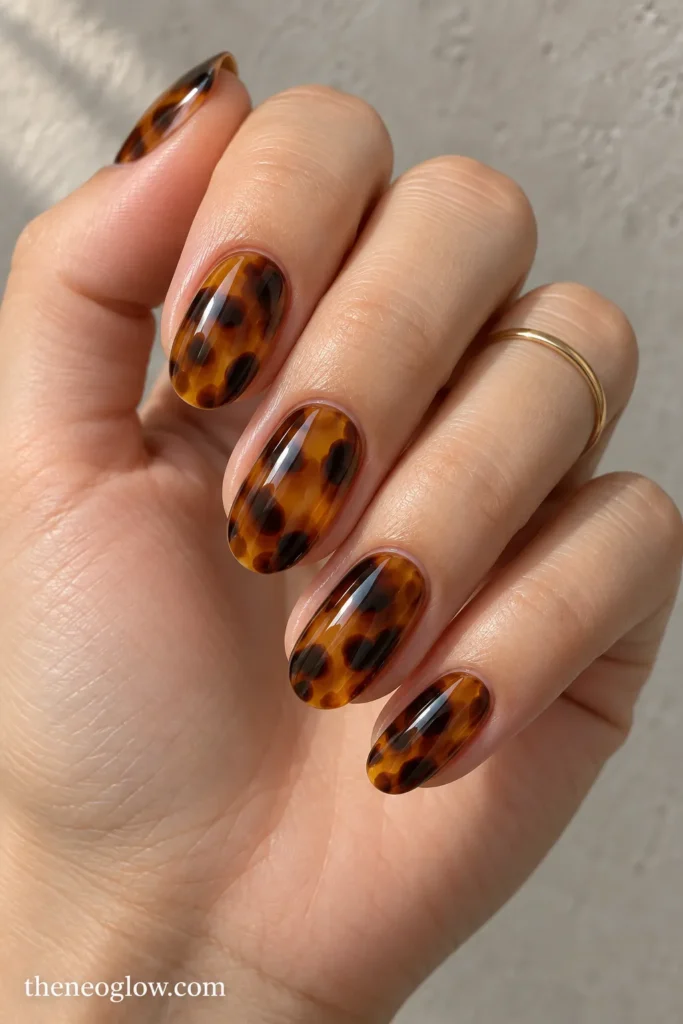 Medium oval nails with glossy translucent amber tortoiseshell, cocoa patches and near-black irregular details.