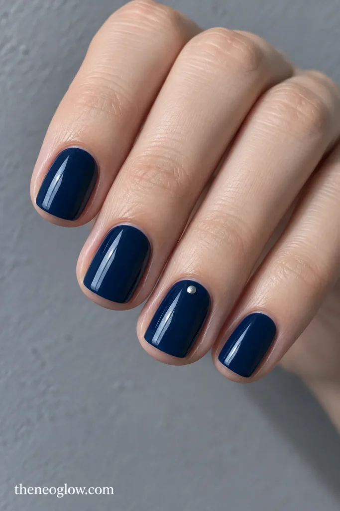 Short soft-square navy nails with one tiny silver dot near the ring-finger base.