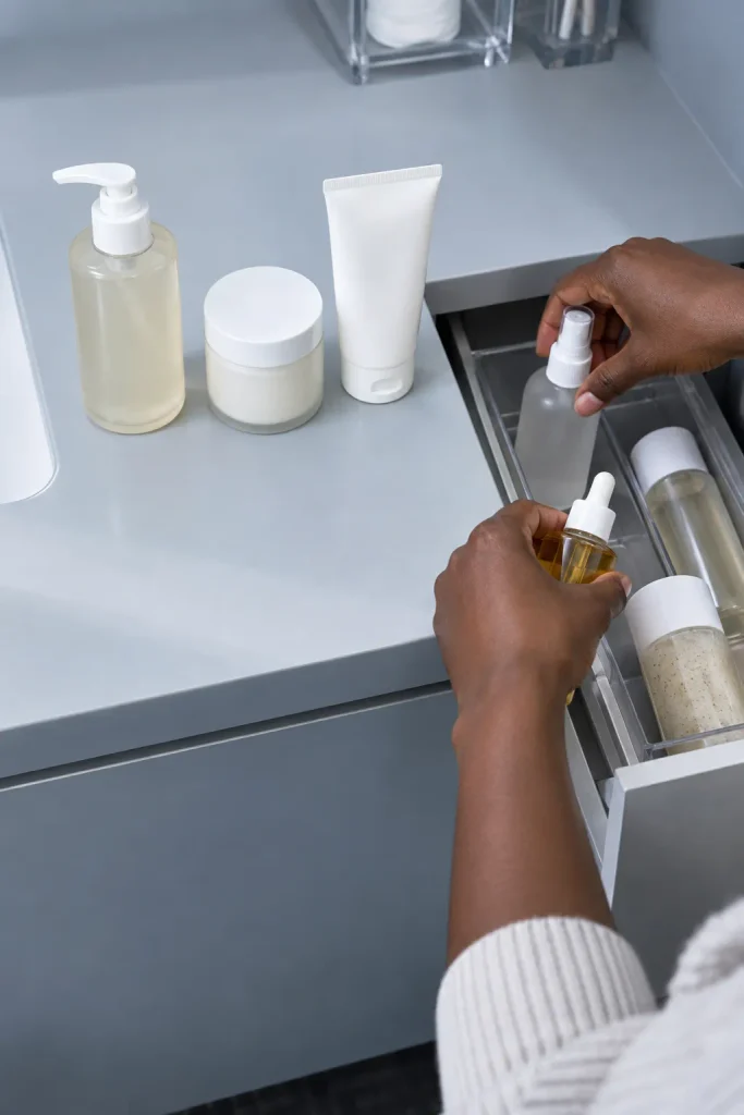 Hands removing extra products from a crowded skin care setup and leaving a simple cleanser, moisturizer, and sunscreen routine.