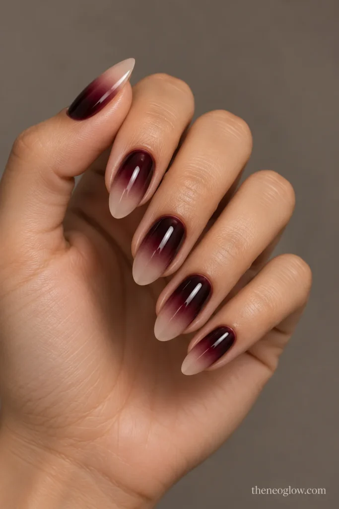 Medium almond nails with black-cherry color fading from the cuticles into sheer neutral tips.