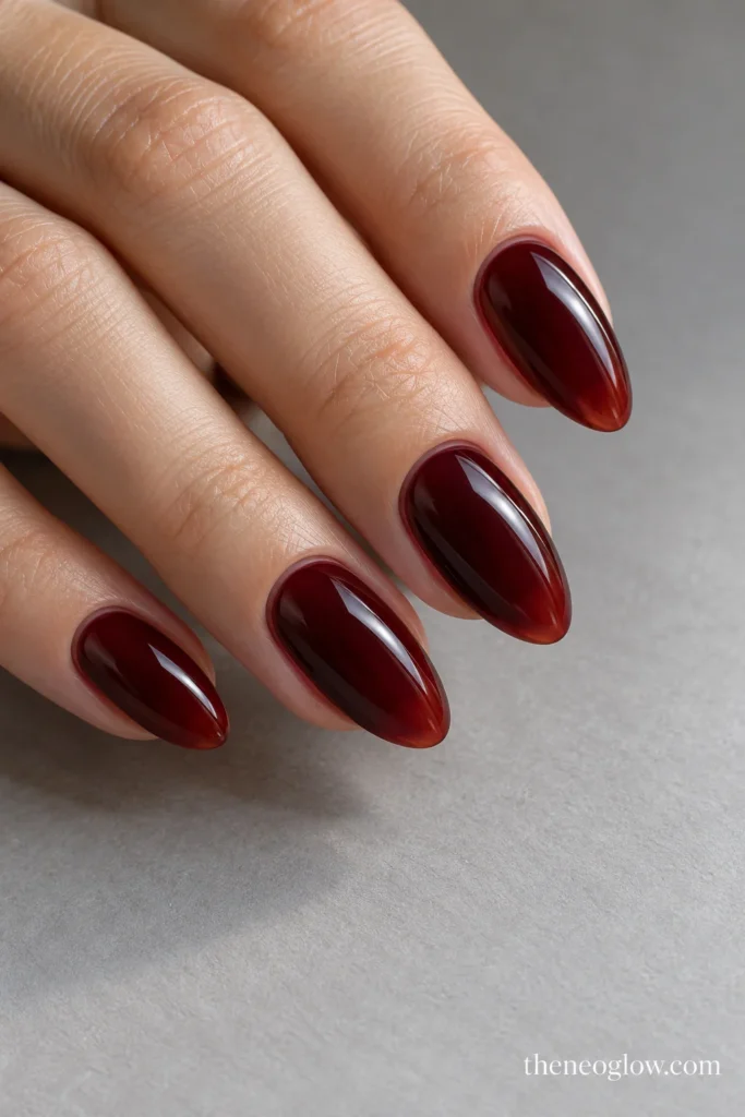 Medium almond nails with translucent black-cherry red-brown jelly polish and glossy depth.