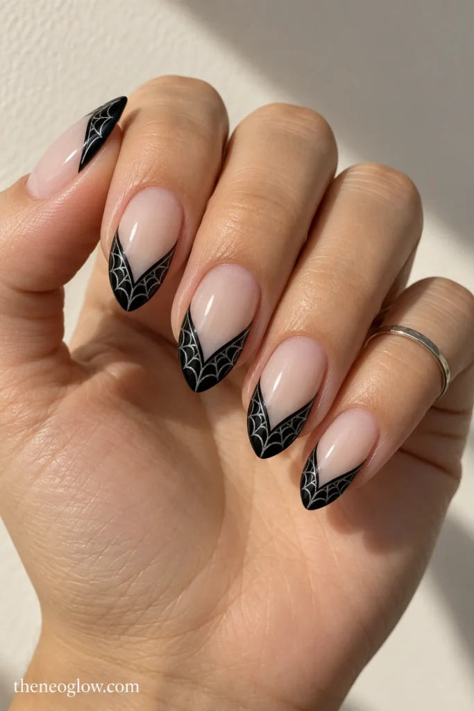 Medium almond nails with black V-shaped French tips containing fine silver-gray spiderweb lines.
