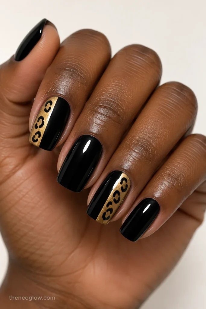 Medium black rounded-square nails with muted-gold side panels and black leopard rosettes on two fingers.