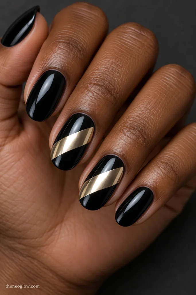 Medium glossy black oval nails with broad diagonal champagne-gold chrome bands on the middle and ring fingers.