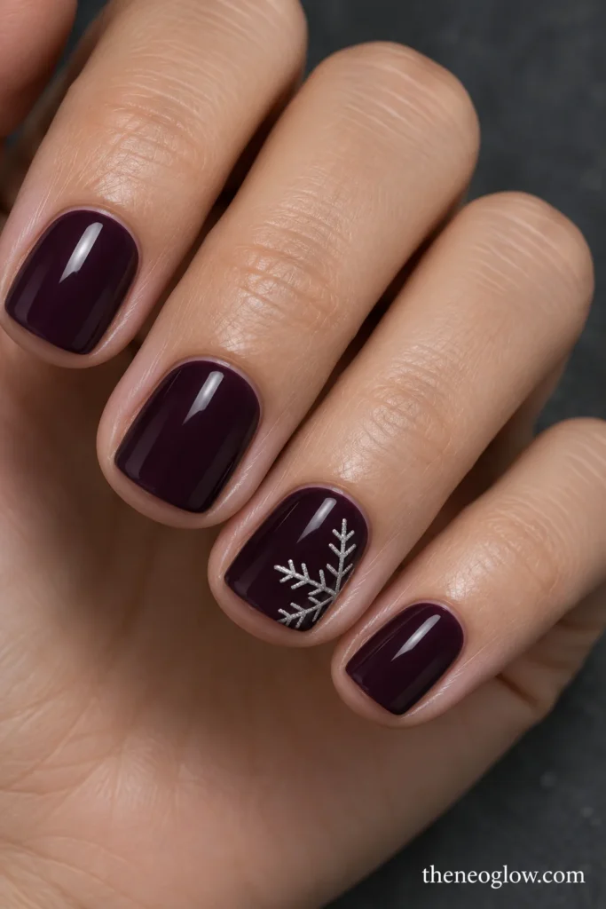 Glossy blackened-plum short square nails with three silver snowflake arms entering one ring-finger corner.