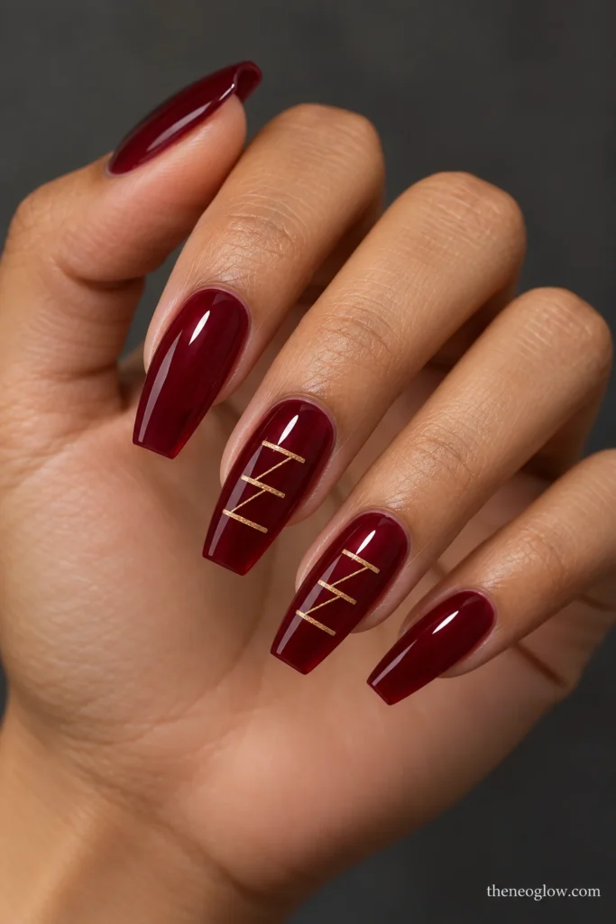 Translucent cabernet-red coffin nails with three short champagne-gold bars linked diagonally on two accents.