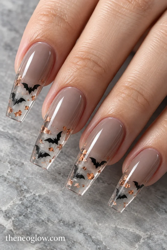 Clear coffin acrylic tips with small black bat silhouettes and scattered copper foil over smoky-taupe bases.