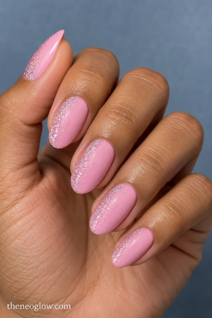 Medium cool-pink oval nails with fine pale-pink glitter fading diagonally inward from one sidewall.