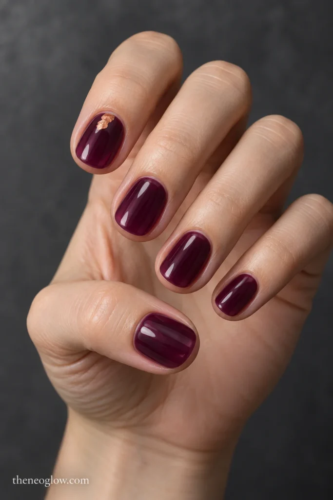 Short translucent plum-jelly round nails with one small reflective copper foil accent near the index-finger cuticle.