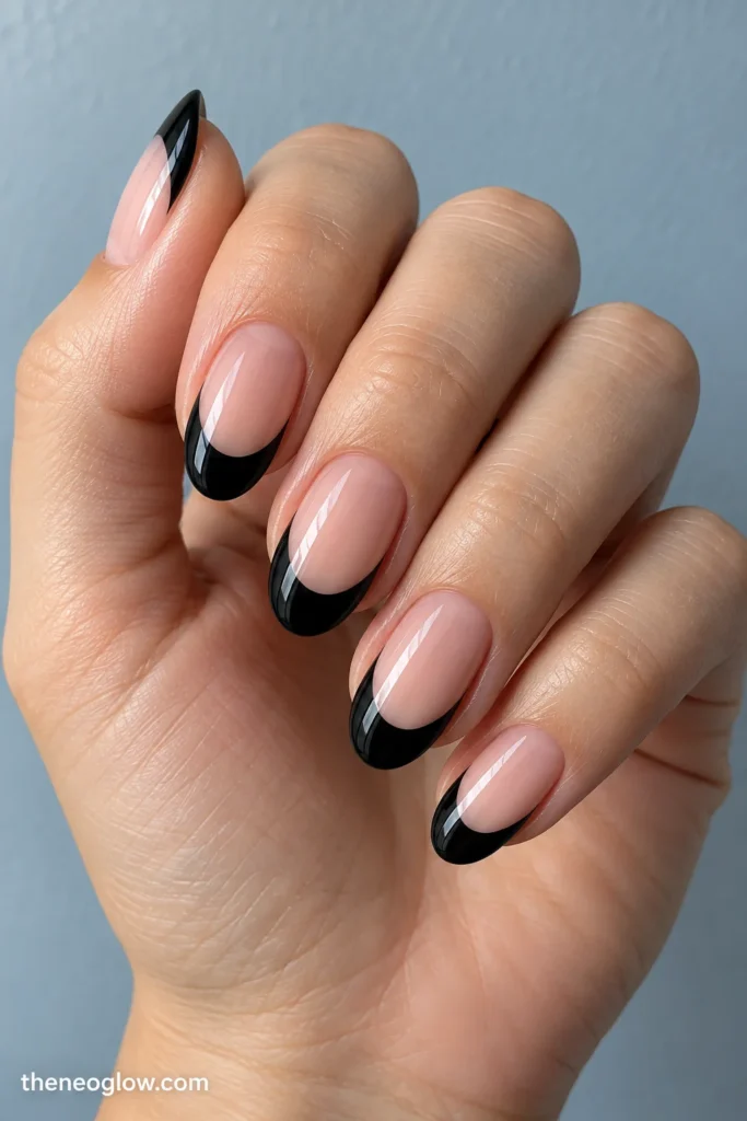 Medium oval nails with deep symmetrical glossy black French tips and sheer peach-pink bases.