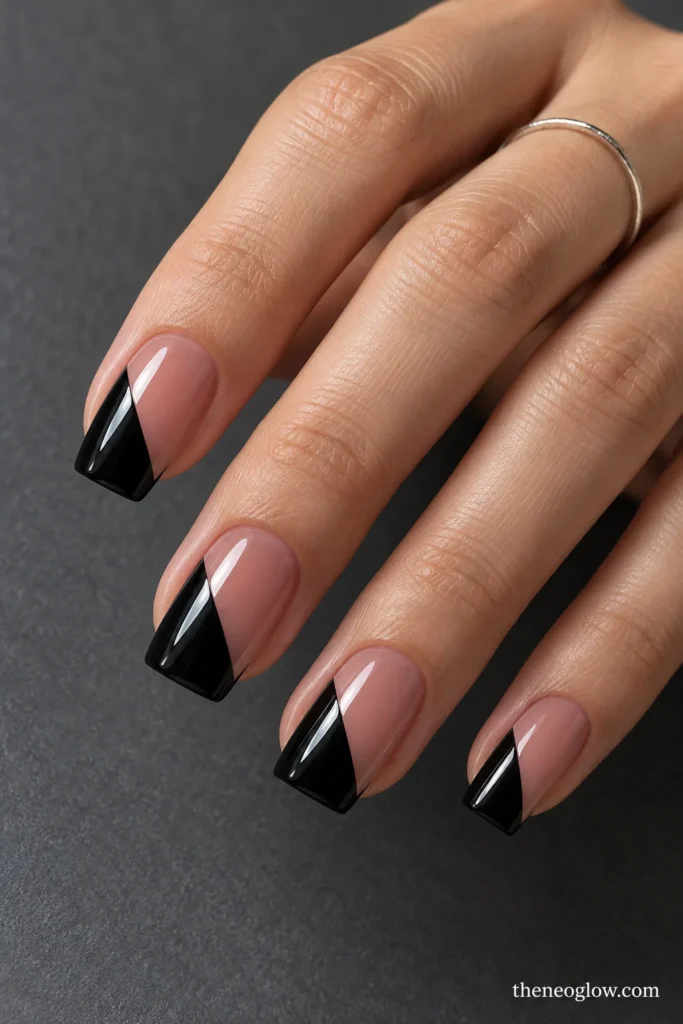 Soft-square nails with sharply angled black triangular French tips over a sheer tan-rose base.