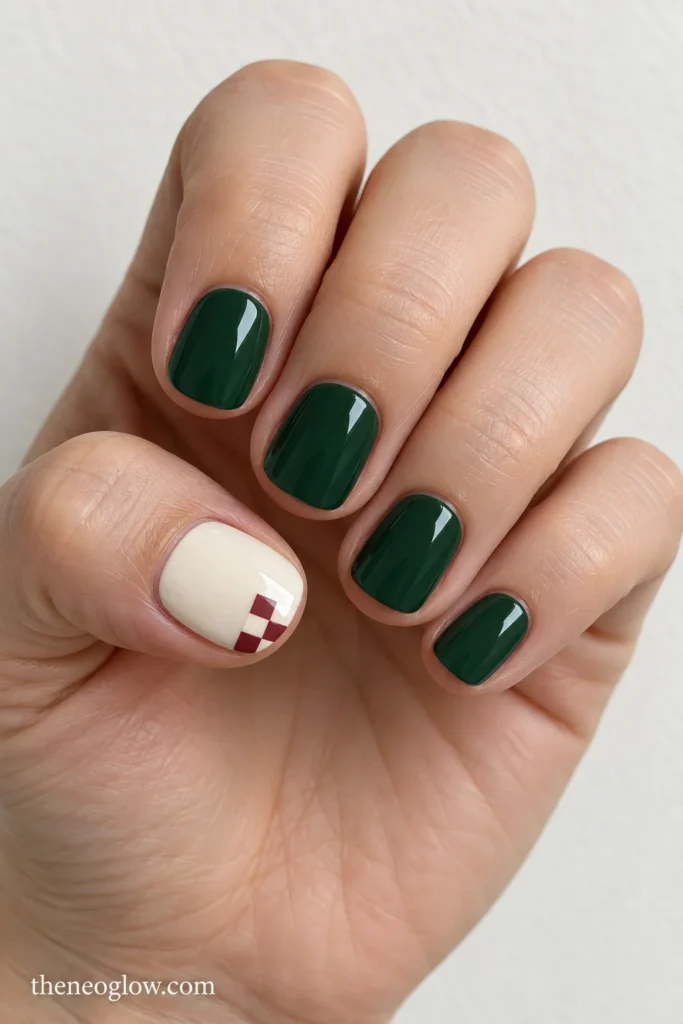 Short glossy forest-green squoval nails with an ivory thumbnail featuring a small cranberry-and-ivory checker patch.