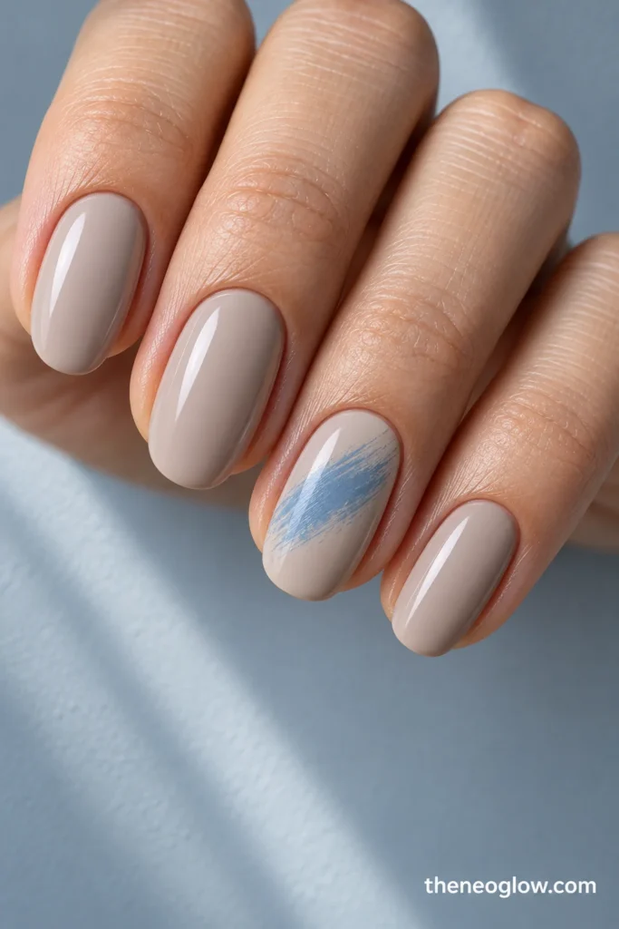 Medium cool-beige oval nails with one irregular frost-blue diagonal dry-brush patch on the ring nail.