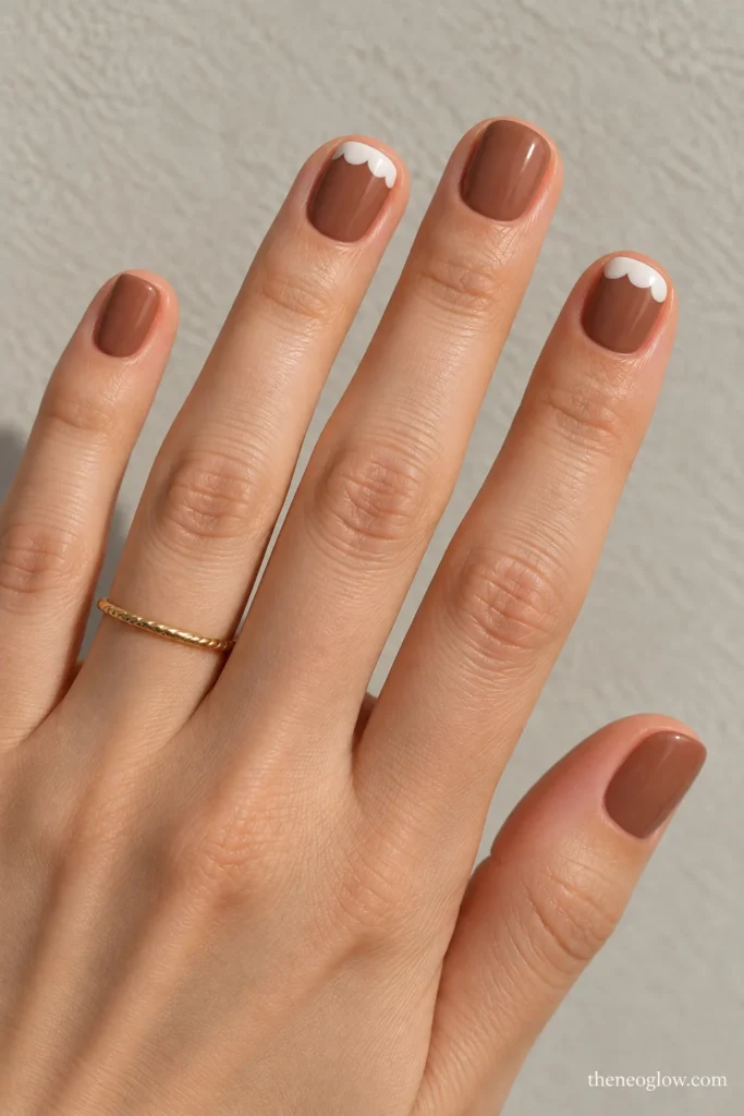 Very short cocoa-brown square nails with white icing-inspired scallops near the index and ring-finger cuticles.