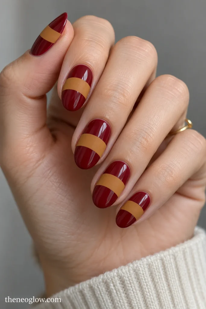 Wine-red oval nails with broad matte ocher arcs across the middle of each nail.