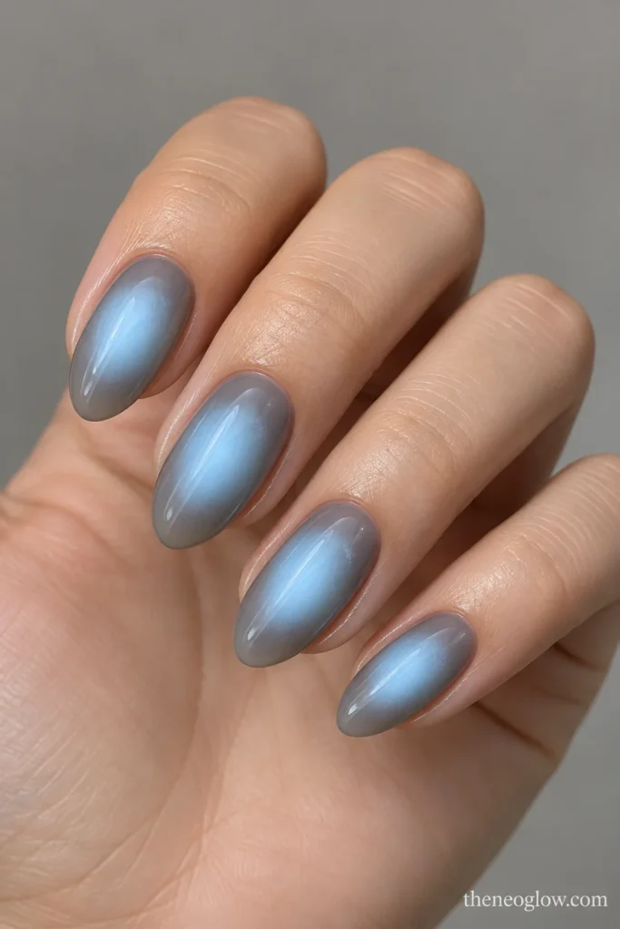 Medium almond nails with diffused icy-blue aura centers over smoky-gray bases.