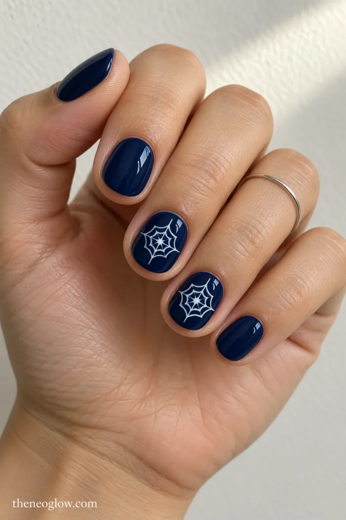 Very short round midnight-blue nails with centered white spiderweb rosettes on the middle and ring fingers.