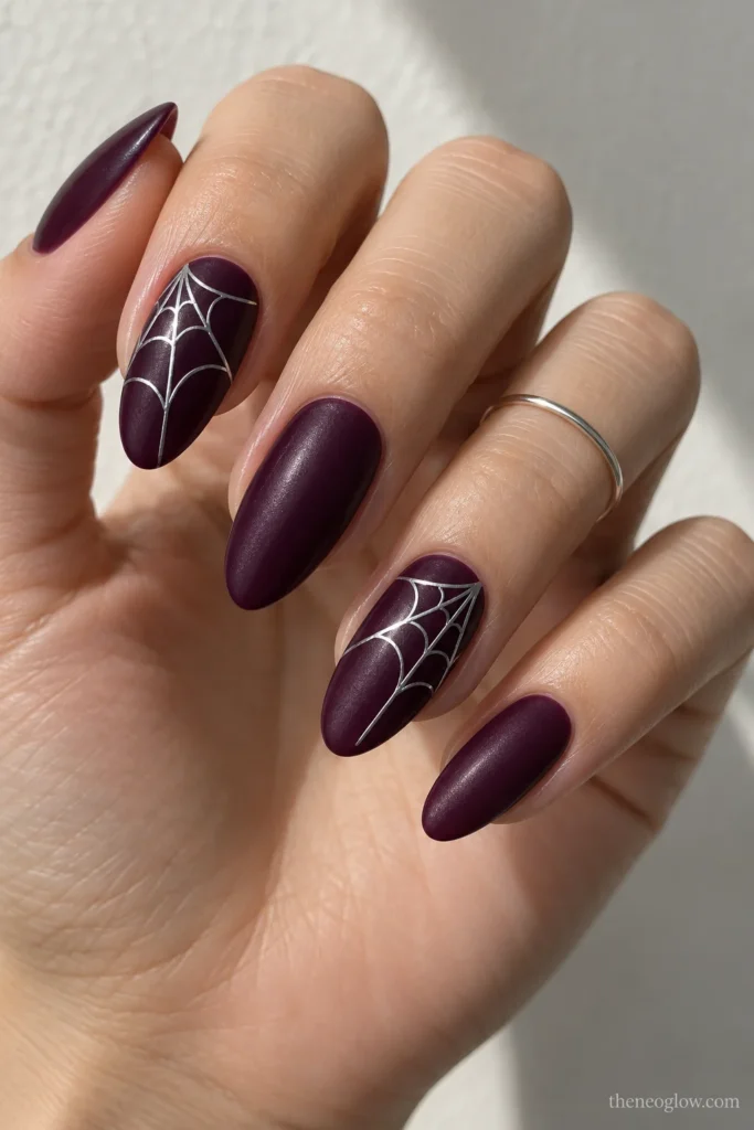 Medium almond plum-satin nails with mirror-silver spiderweb filaments radiating from the outer sidewalls.