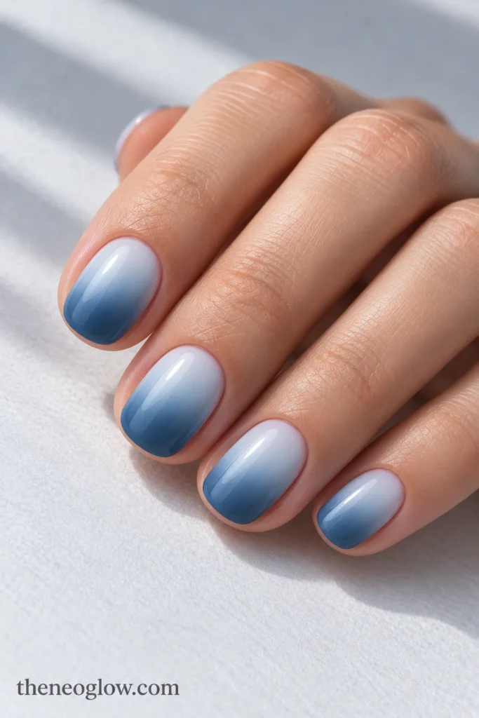 Short rounded acrylic nails fading smoothly from misty pale blue at the base to steel blue at the tip.