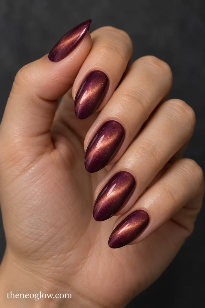 Deep mulberry almond nails with soft amber-rose magnetic cat-eye highlights.