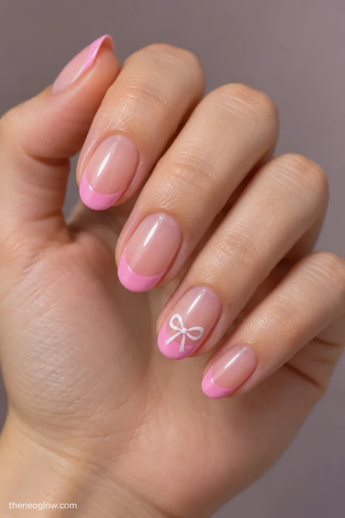 Medium oval nails with glossy bubblegum-pink French tips and one tiny white bow on the ring finger.
