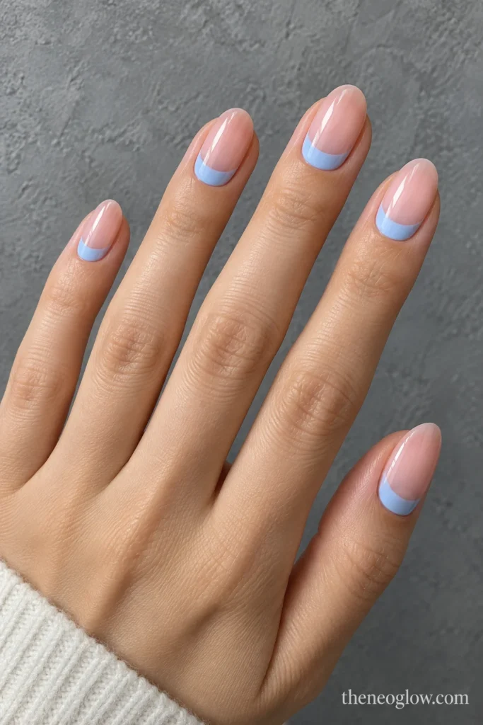 Medium oval nails with powder-blue cuticle crescents over sheer neutral-pink polish.