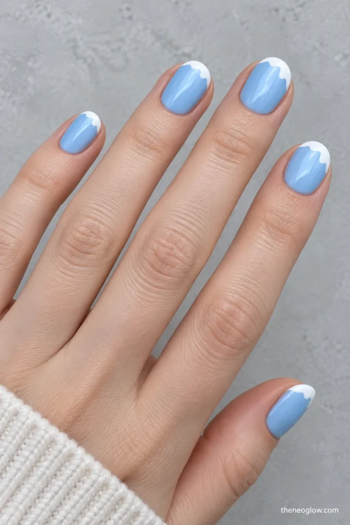 Short oval nails painted powder blue with irregular white snowcap details along the outer tips.