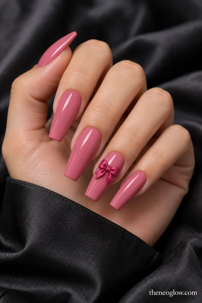 Long glossy rose-pink coffin nails with one small raised raspberry satin bow on the ring finger.