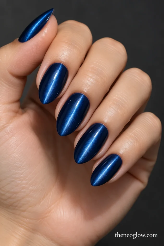 Medium almond nails with sapphire magnetic polish and narrow centered cat-eye beams.