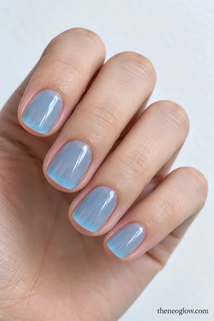 Short round nails with translucent icy cyan-blue jelly polish and a glossy finish.