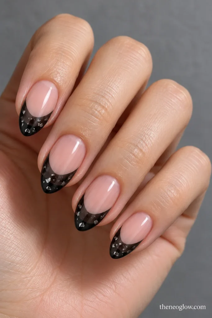 Almond nails with translucent smoky-black jelly French tips containing scattered tiny silver flakes.
