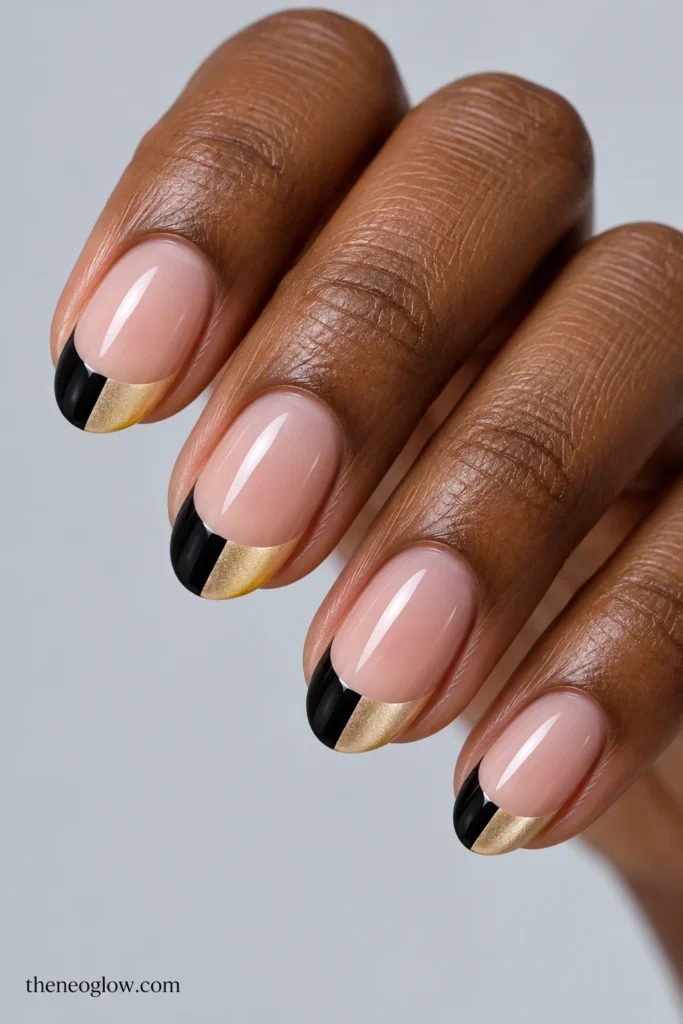 Medium oval nails with neutral-pink bases and French tips divided into black and pale metallic-gold halves.