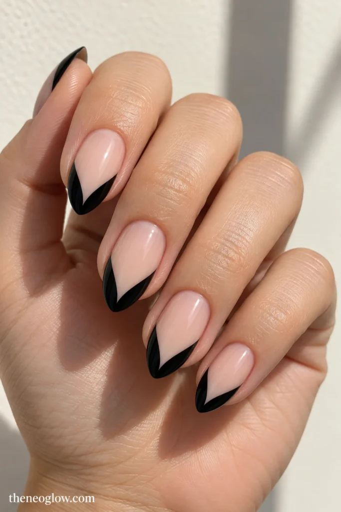 Medium almond nails with symmetrical glossy black V-shaped French tips over milky pink.