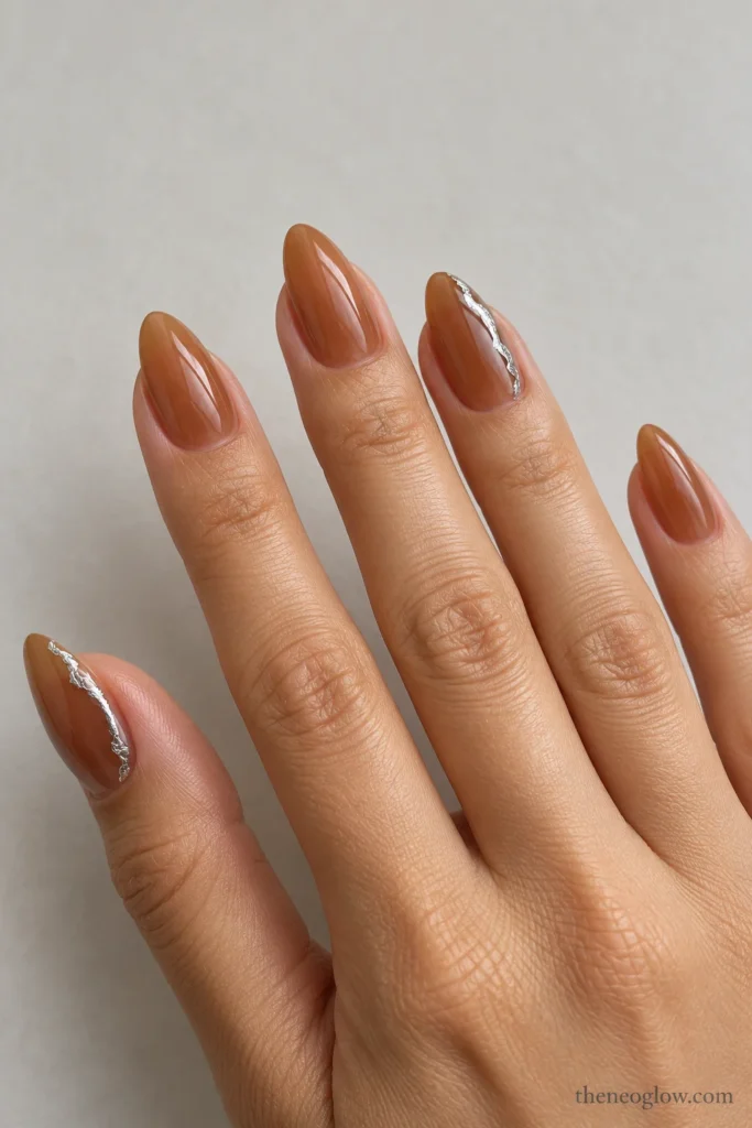 Translucent warm-toffee almond nails with flat irregular pewter-foil side borders on the thumb and ring finger.